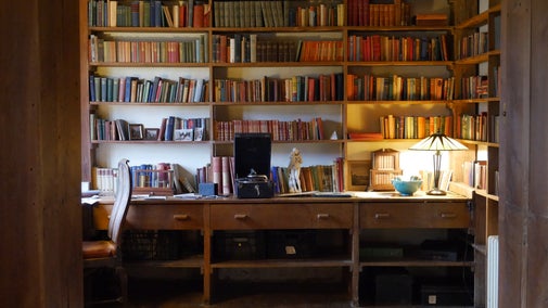 Books line a series of wooden shelves in a small study